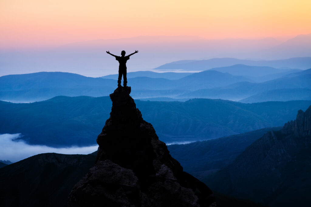 man on top of the mountain looking to the sun