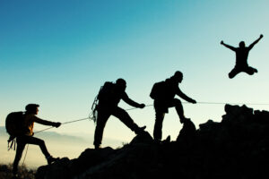 4 Travellers silhouette climbing up a mountain with one traveller jumping up celebrating