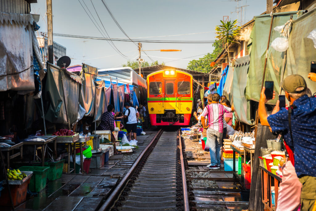 Train on Tracks Moving Slow. Umbrella Fresh Market on the Railroad Track, Mae Klong Train Station, Bangkok, Thailand on a Sunny Day.