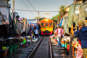 Train on Tracks Moving Slow. Umbrella Fresh Market on the Railroad Track, Mae Klong Train Station, Bangkok, Thailand on a Sunny Day.