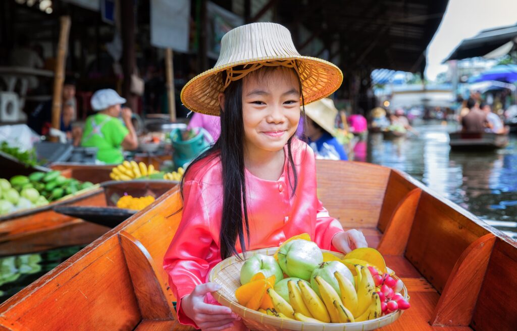 Child sit on the boat and hold the fruit basket in Traditional floating market , Thailand