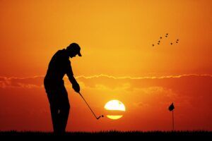Golfer at sunset swinging there putter with the flag seen in the distance