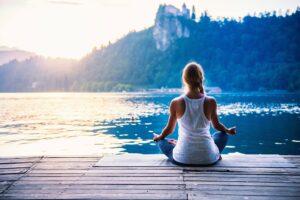 A Woman doing Yoga on a pier with sunshining upon the water Infront of her